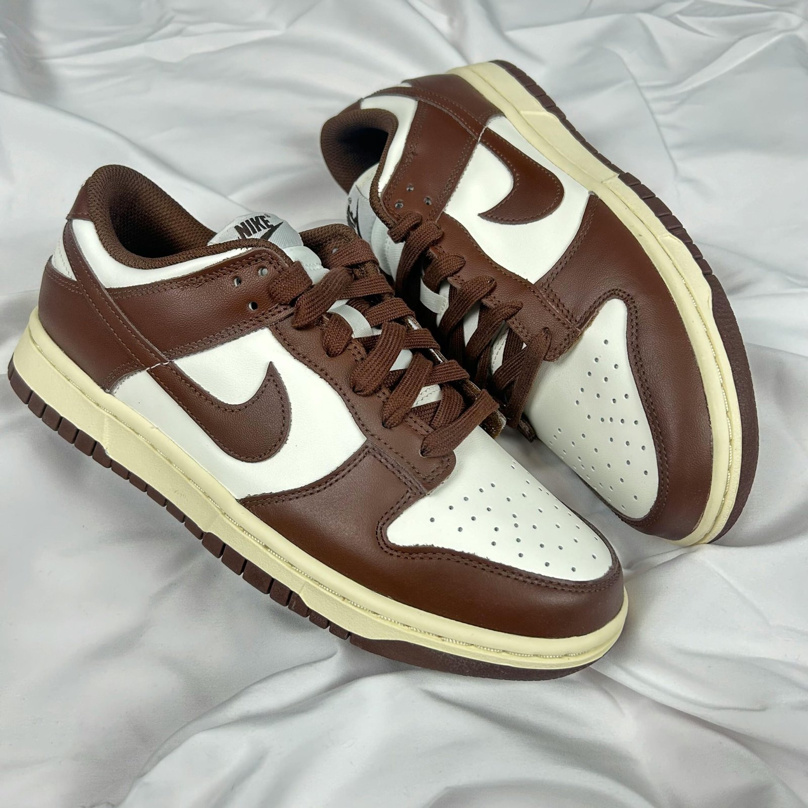 Stylish Nike Dunk Low sneakers in brown and white leather displayed on a white fabric.
